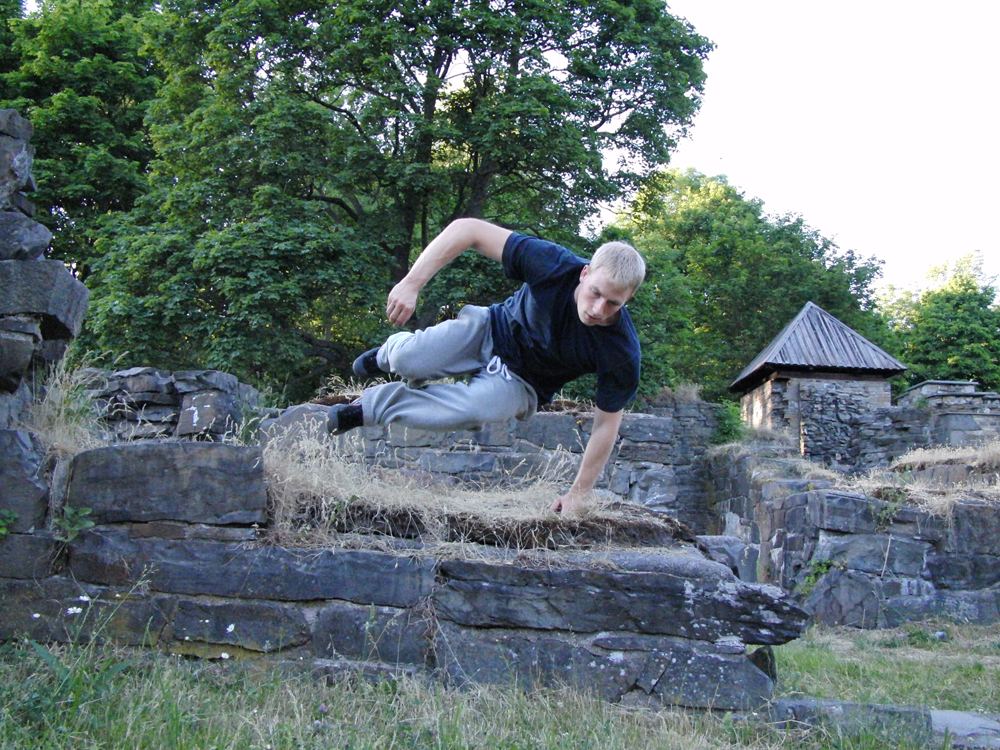 A traceur clearing a low stone wall with a speed vault