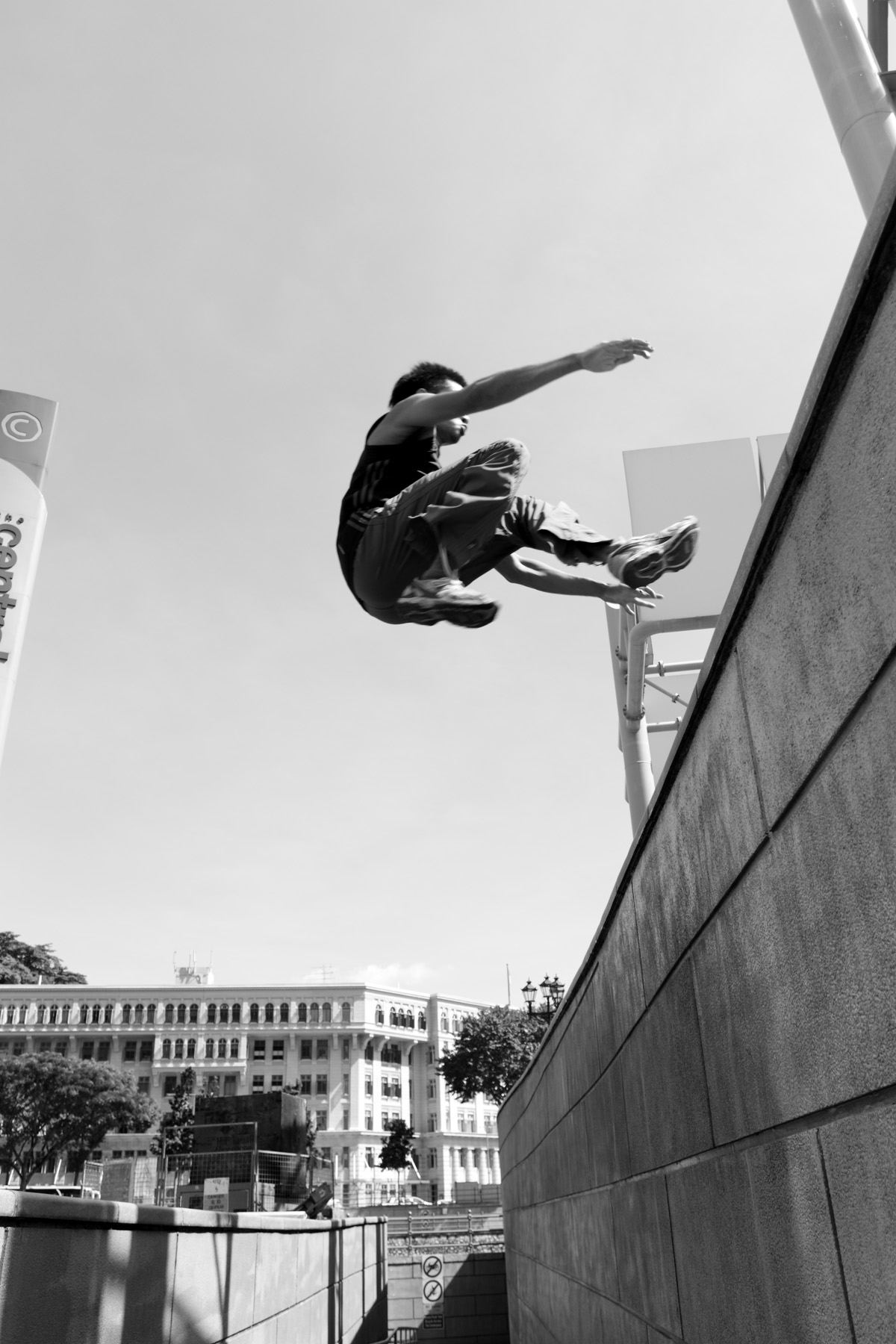 Black and white photo of a parkour athlete in flight beside a tall wall
